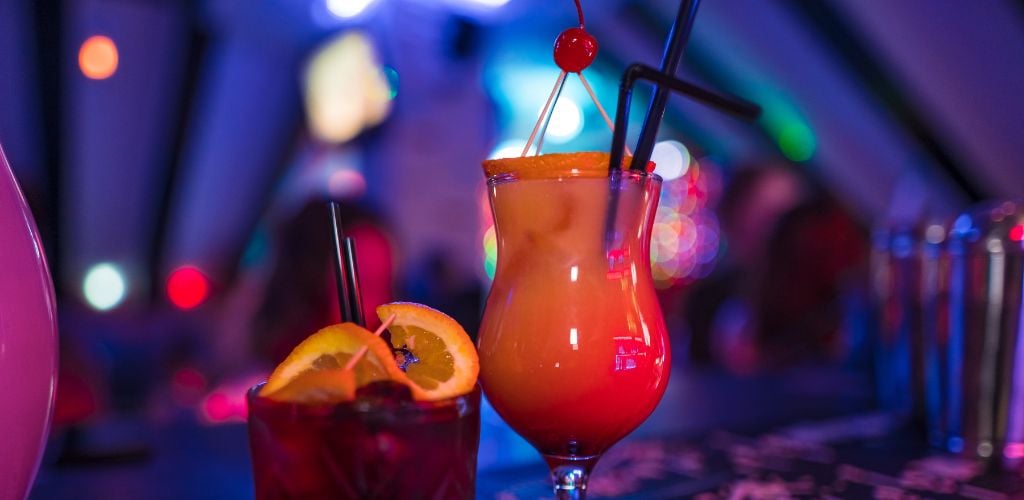 two glasses of cocktail with cherry on top and the other glass has orange on the top.