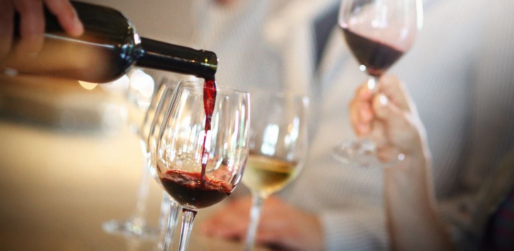 Pouring a wine in a wine glass with a number of other wine glasses in the background.