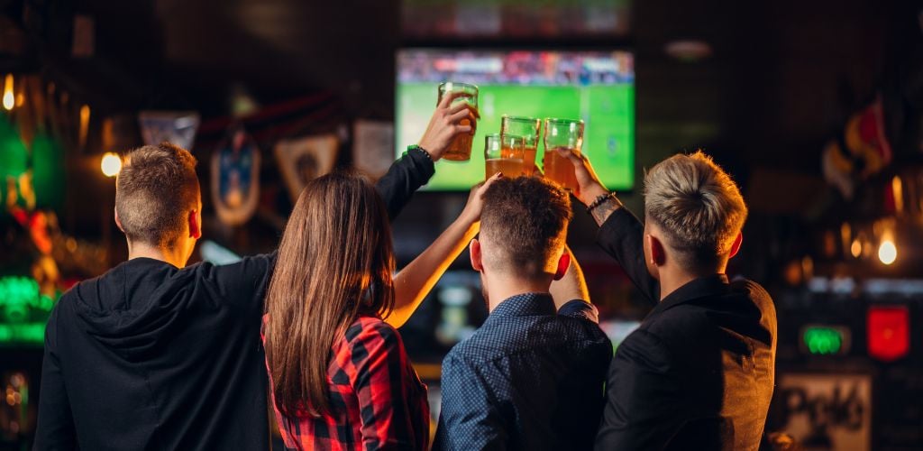 Four friends are enjoying four glasses of beer and toasting at the sport bar.