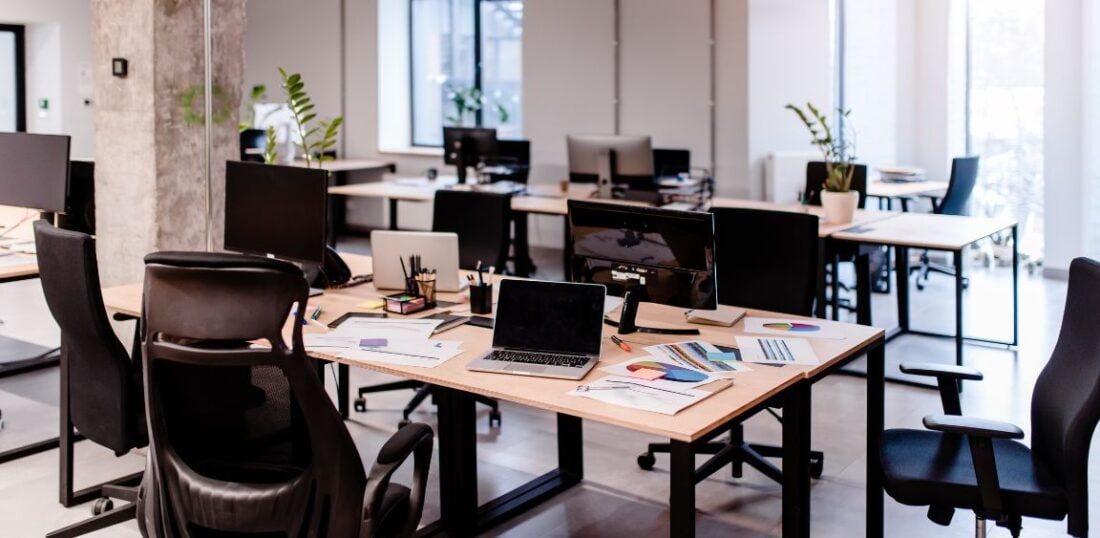 image of a shared office space with multiple desks, office chairs. Laptops and paperwork on desks 