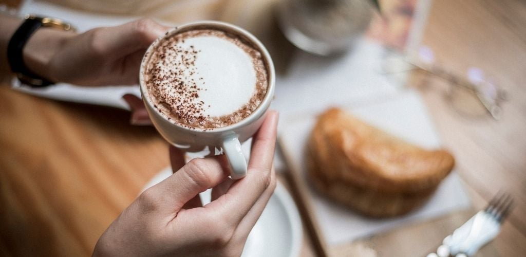 coffee being held and pastry on table 