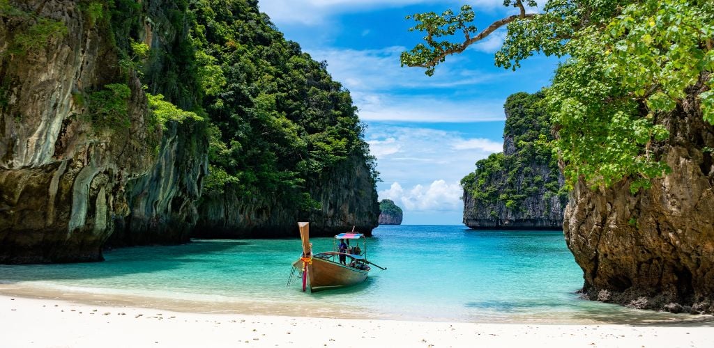 Phi Phi island in Thailand, white sand beach and beautiful blue water with rocky backdrop and local boat.
