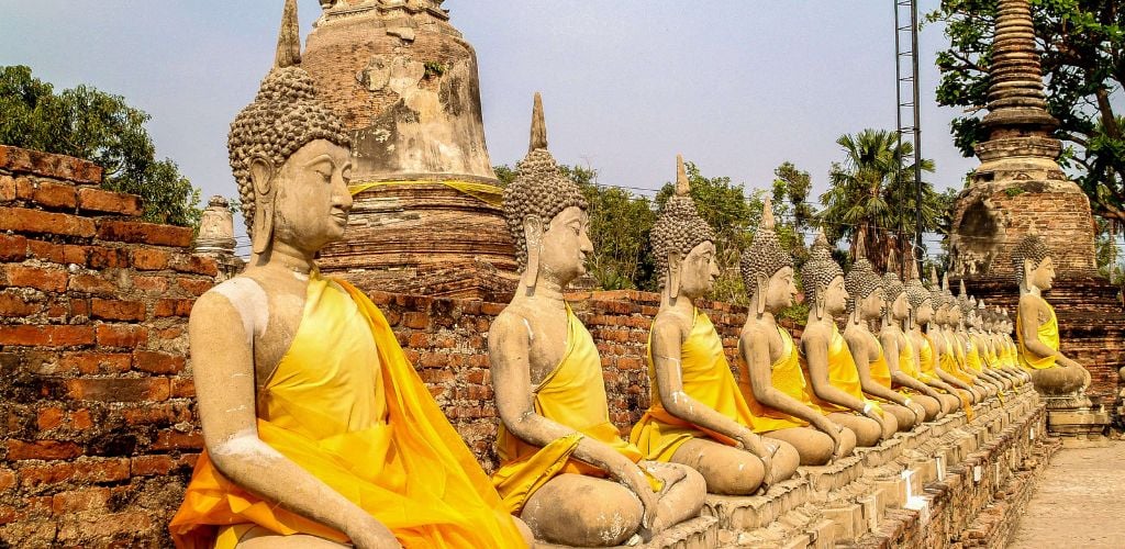 Ayutthaya Historical Park Thailand, row of buddha statues with clear blue skies and surrounding palm trees