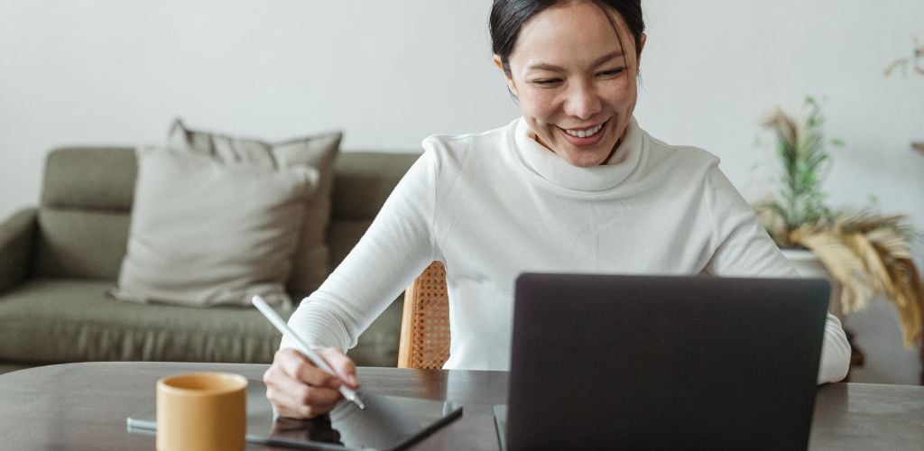 joyful woman working from home with laptop and drawing tablet 