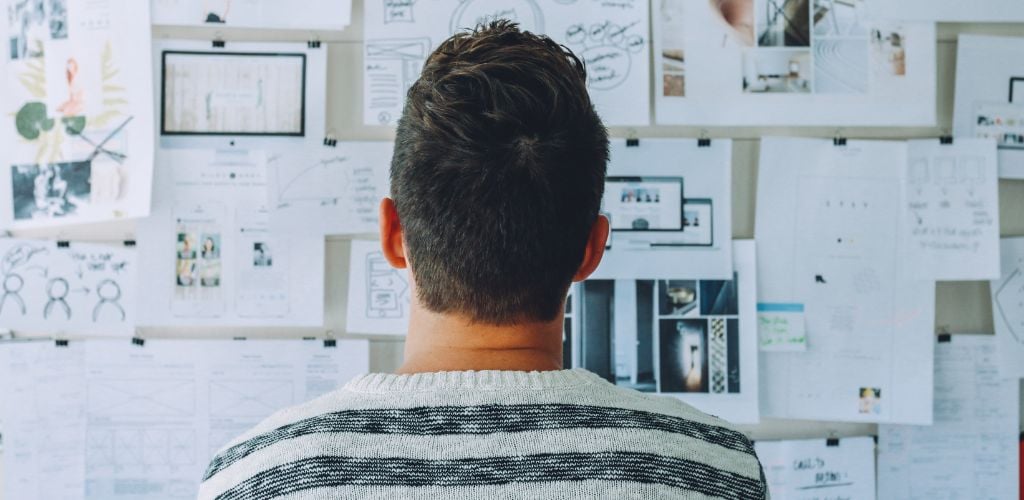 man looking at a large vision board of ideas, business plans, post-it notes and images 