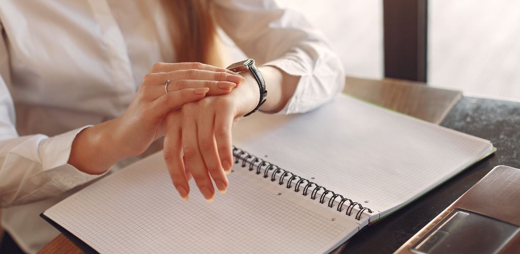 time management, person looking down at watch whilst working with an open notepad 