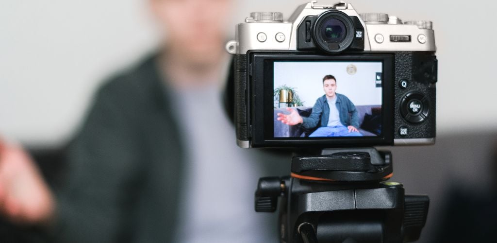 man sitting on sofa with recording camera set up on tripod in foreground 