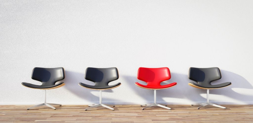 representation of unique, four chairs in a row, all the same style but one red, others are black 