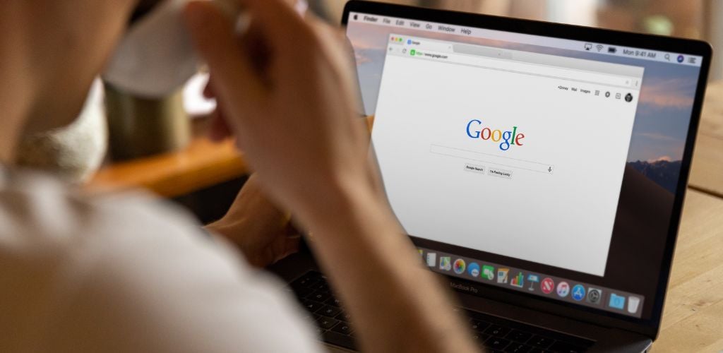 laptop screen with google homepage on display, person sipping from a coffee mug 