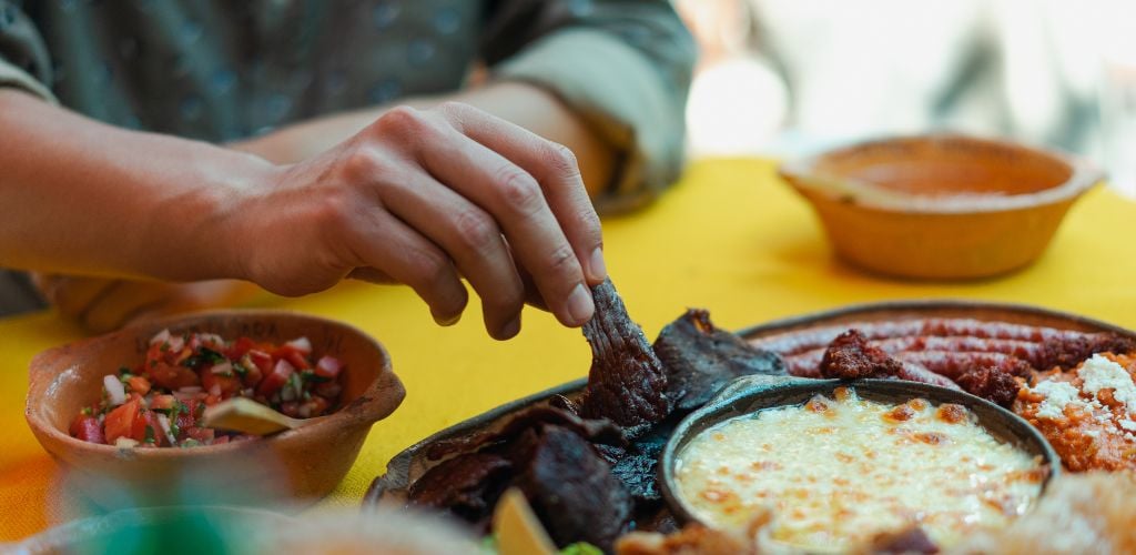 Person Eating Mexican Food, side dish of salsa and cheese dipping sauce in centre of dish served with meat 