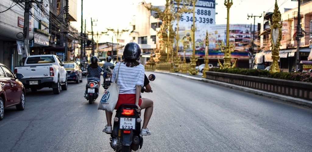 motorcycle scooter riding through city environment, passenger holding on to back of bike