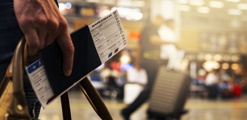 person walking through airport lounge with passport and boarding pass in hand with carry on bag