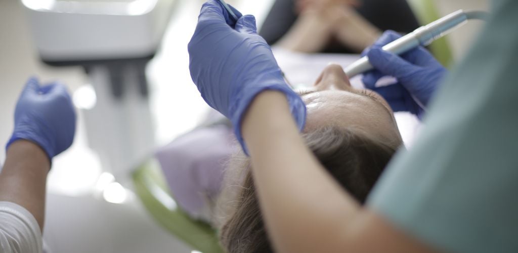 dental visit, dentist using dental instruments on patient who is laying down in the treatment chair 