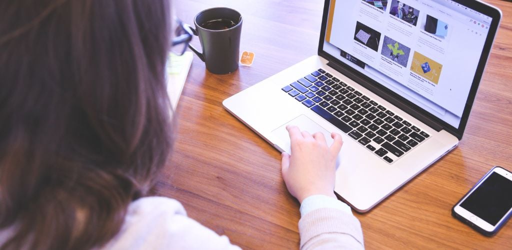 person looking at a website on a laptop. Mug of tea on desk, mobile phone beside laptop