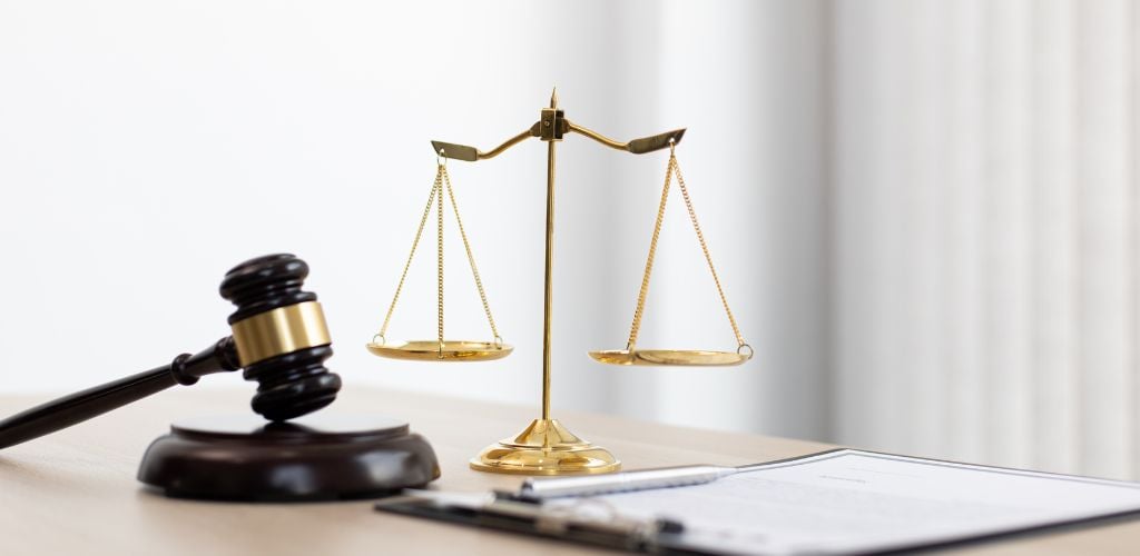 paper documents on clipboard on desk, scales and wooden hammer to represent law 