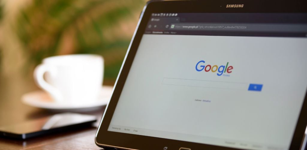 tablet device on desk with google homepage on screen, coffee mug on desk beside smartphone 