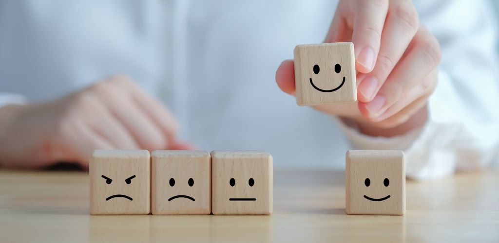 customer service experience, wooden blocks on desk with different facial expressions, person holding up block with smiley face