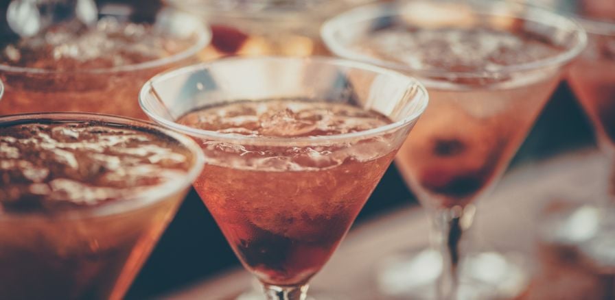 Cherry coloured cocktails lined up on a bar in margarita glasses with ice