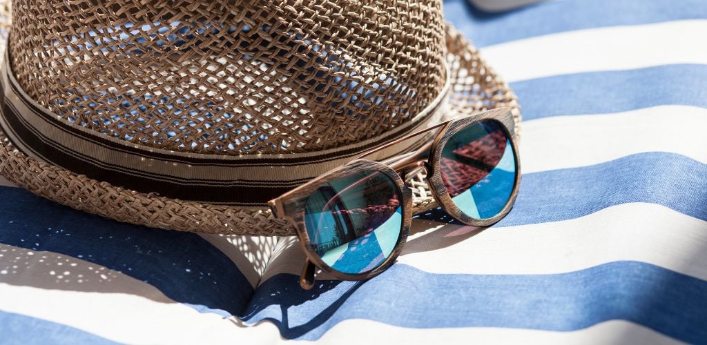 Brown Summer Hat on blue and white Beach Towel with Wooden Sunglasses