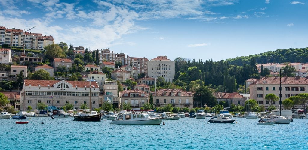 View of Dubrovnik, Croatia from the sea, looking towards buildings that line the hillside and cliffs