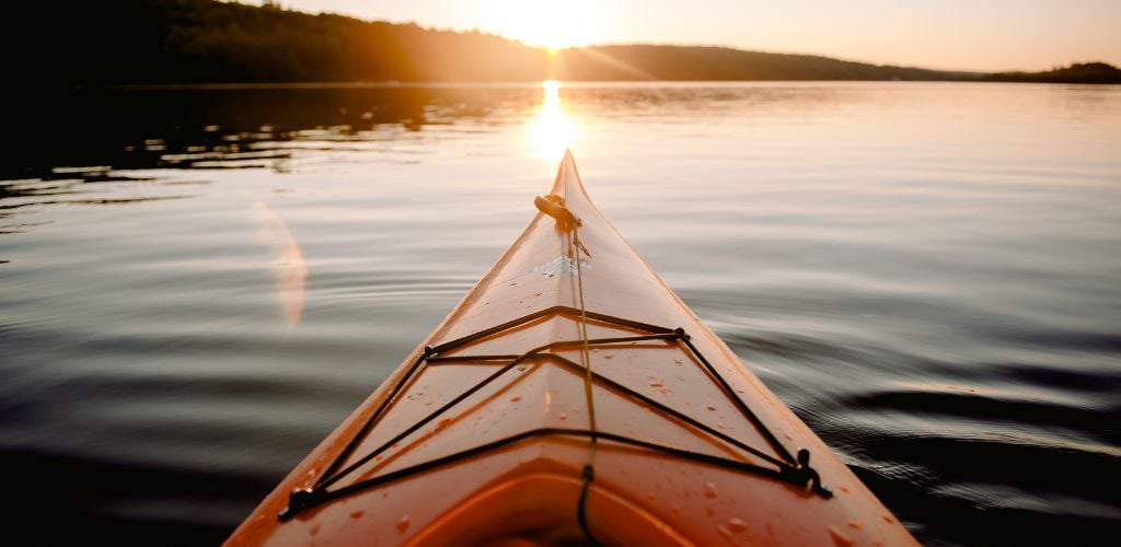 Kayak on open water during sunset time, sun setting towards horizon 