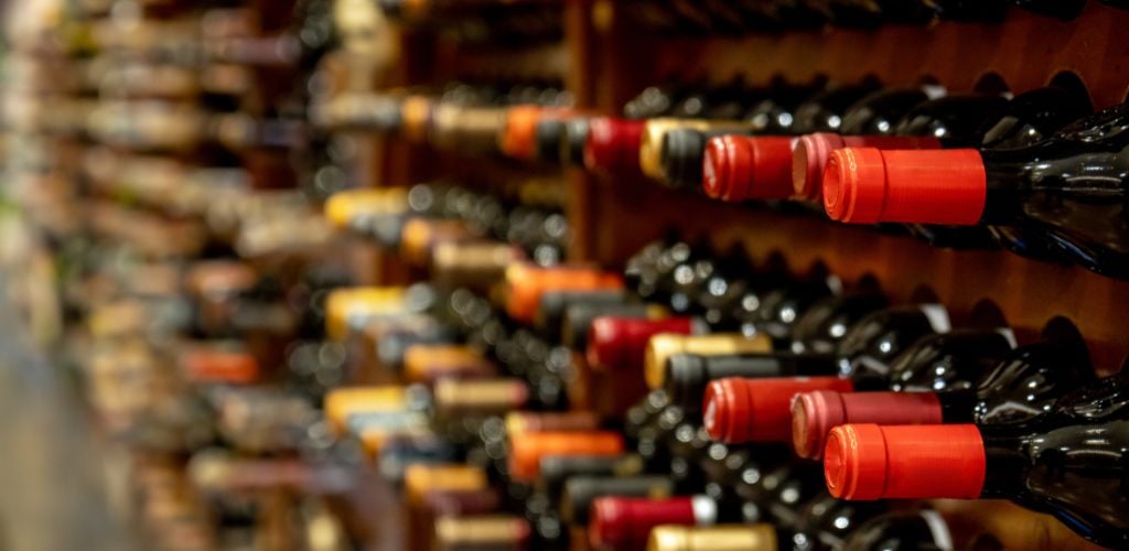 Bottles of black red wine lined up and stacked on wooden wine rack shelves in a wine cellar 