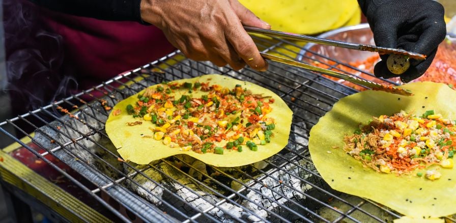 Grilled vietnamese pancake with eggs, sausages and sauces in Vietnam, vendor preparing an order with cooking tongs 