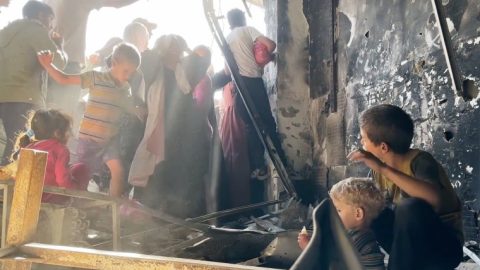 As crowds surge for bread in Gaza, a boy helps his younger brother to drink