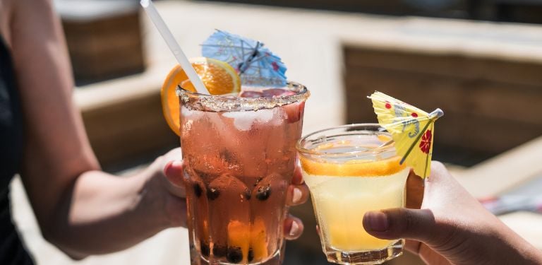 Two people holding drinking classes in a cheers, both with cocktail umbrellas and slices of citrus 