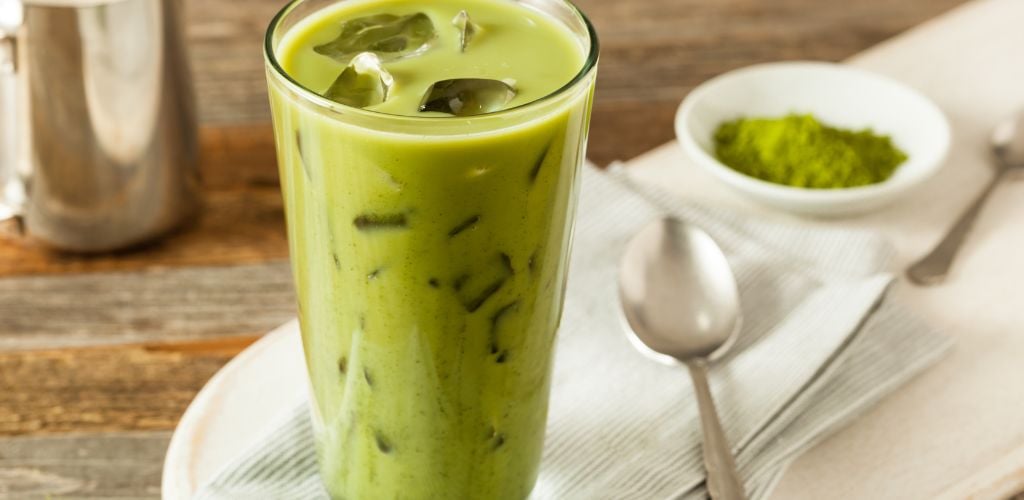 matcha latte in glass tumbler with small spoon to side and machca powder 