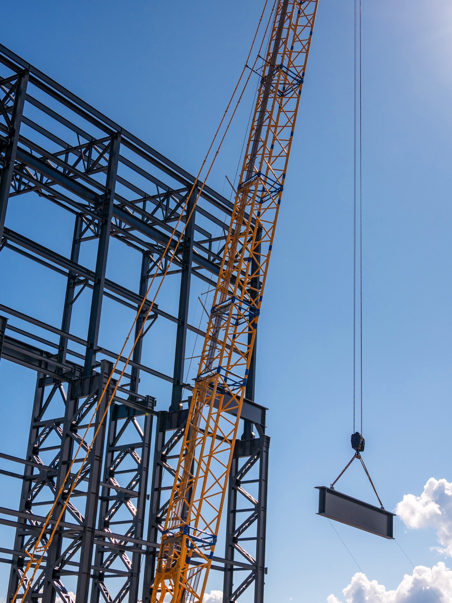 crane hoisting an i-beam next to a steel building frame