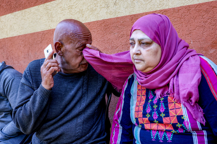 Palestinian man wipes his eyes with his wife's headcovering.