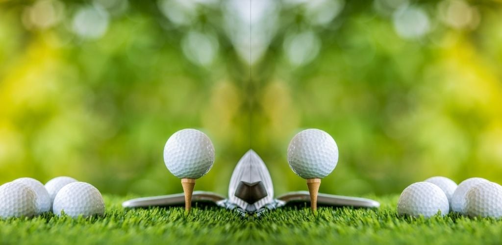 mirror image of golf ball on tee ready to practice, more golf balls on lawn to side of tee