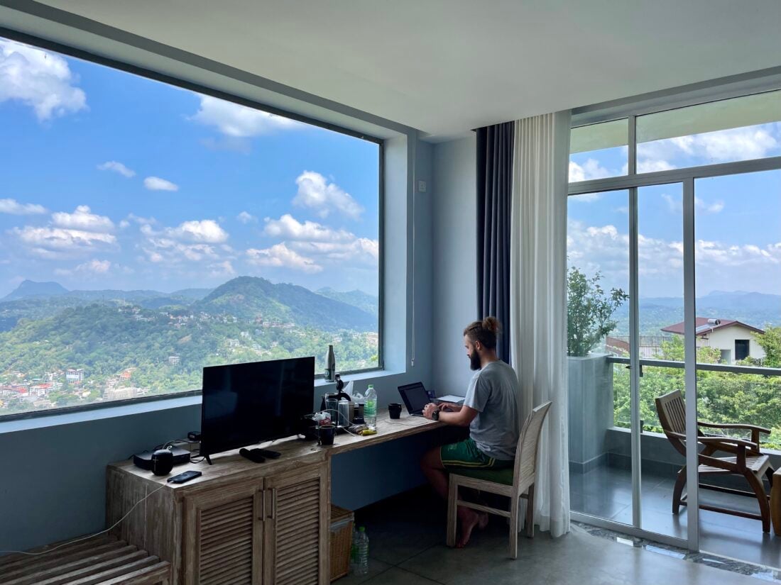 Remote worker Alex working from beautiful location. Working on laptop from desk with surrounding mountain views