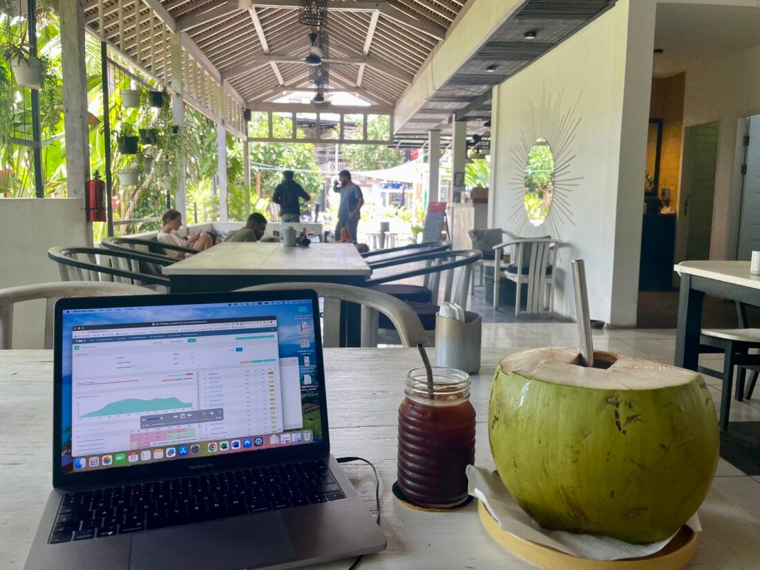 digital nomad set up from a cafe, coconut and coffee on table with open laptop