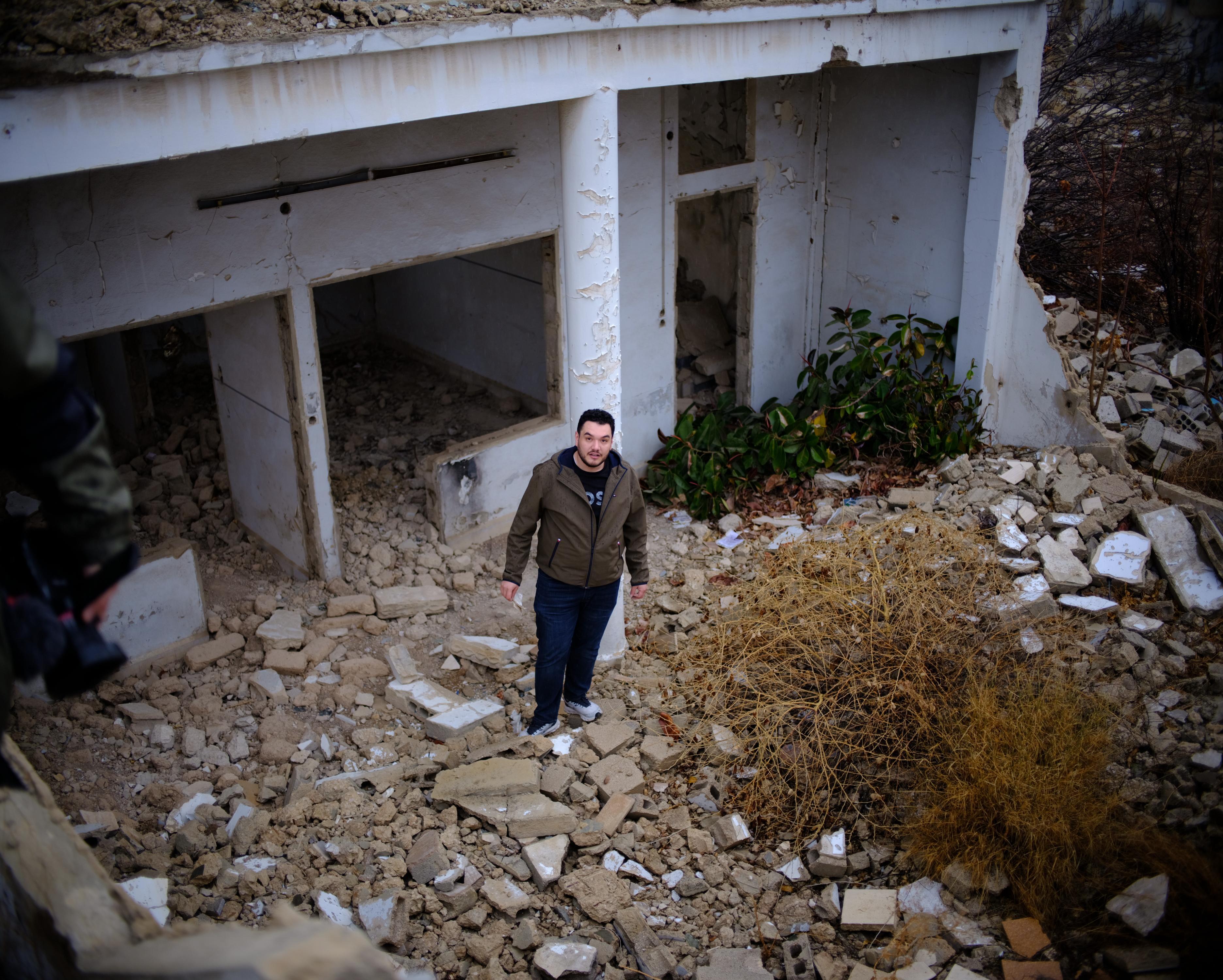 Abdulwahab Omira, 28, stands in front of his destroyed family home in Damascus, Syria. Omira and his family fled Syria